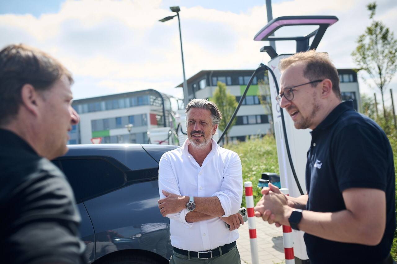 Three men talk by an electric vehicle charging station.